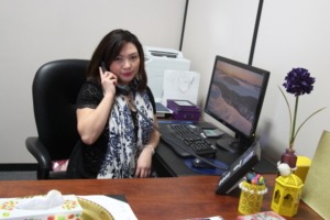 A woman sitting in her office, holding and engaged in a phone conversation.